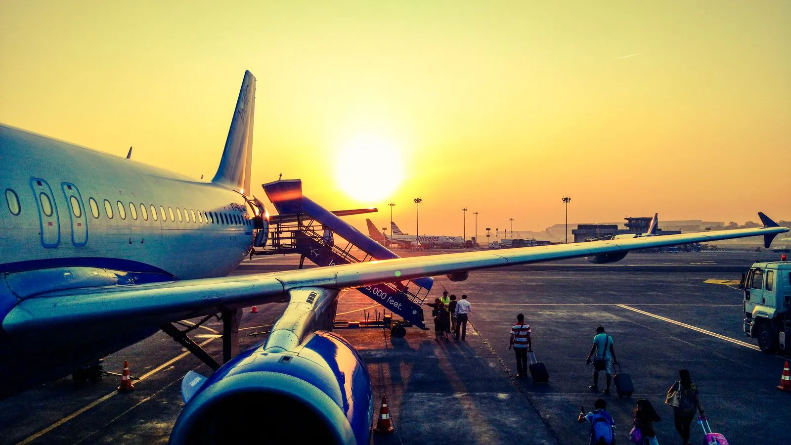 Airline passengers walk across the tarmac with luggage toward a parked jet at sunset