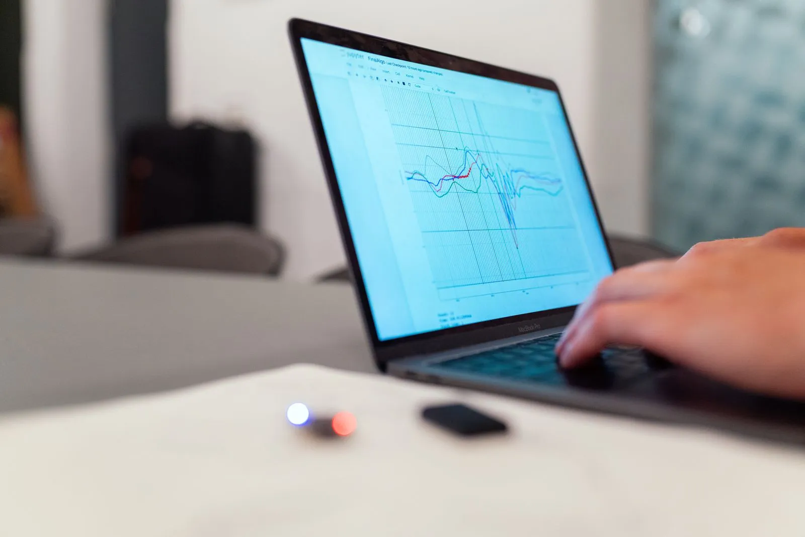 Hand typing on a MacBook Pro displaying a Jupyter notebook with overlapping line-chart data