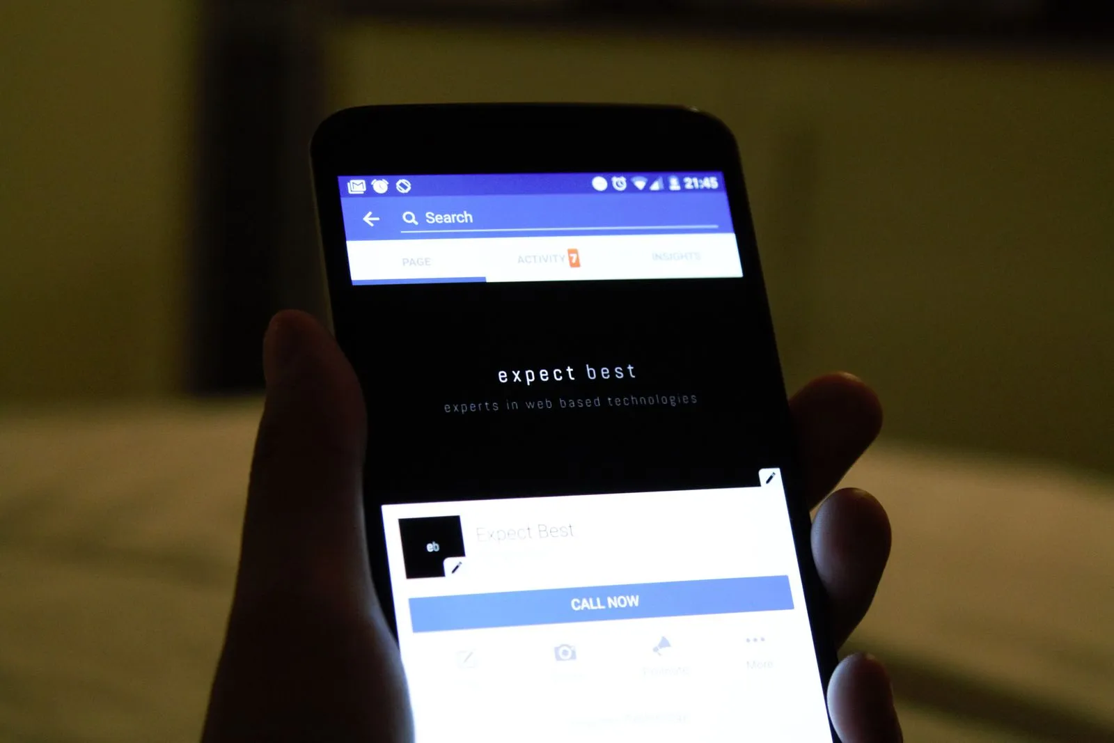 Hand holding a phone showing a business's Facebook page in a dim room