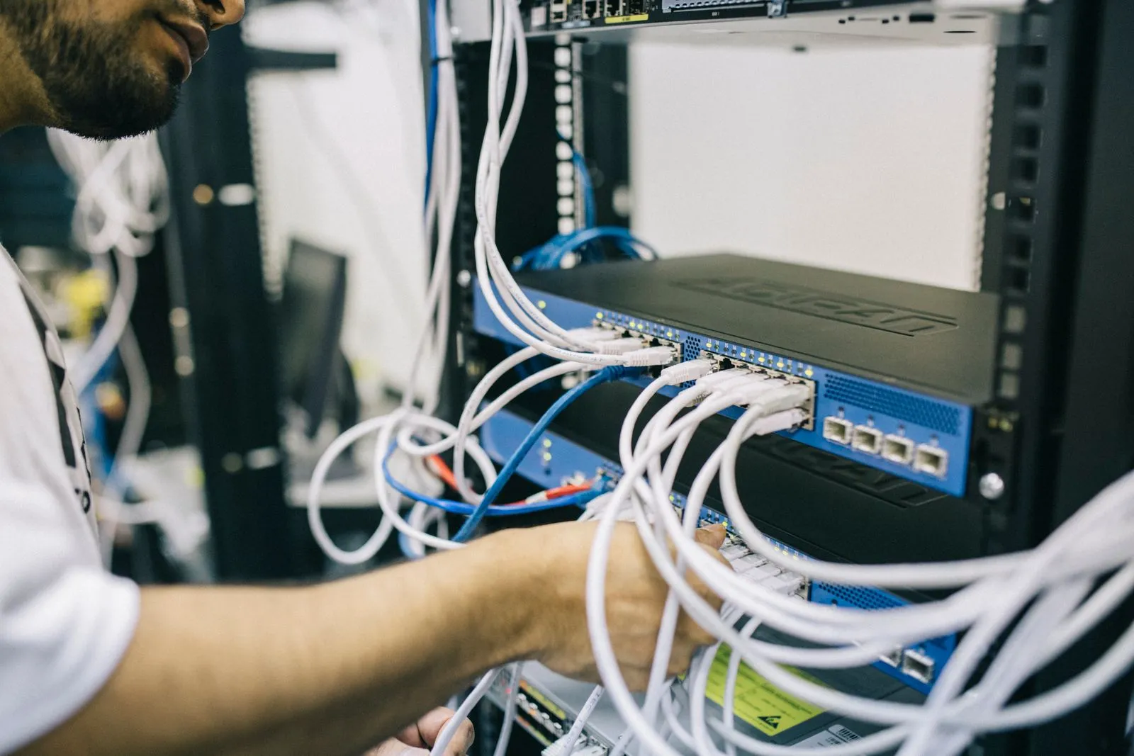 Man plugging ethernet cables into a network switch mounted in a server rack