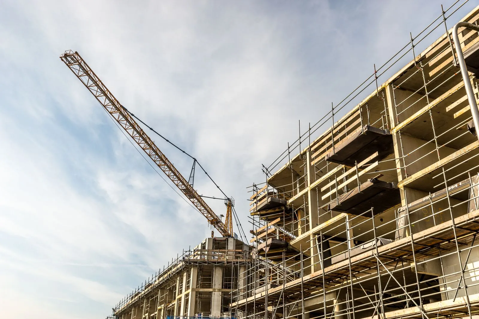 Low-angle view of a tower crane beside a multi-story building wrapped in scaffolding