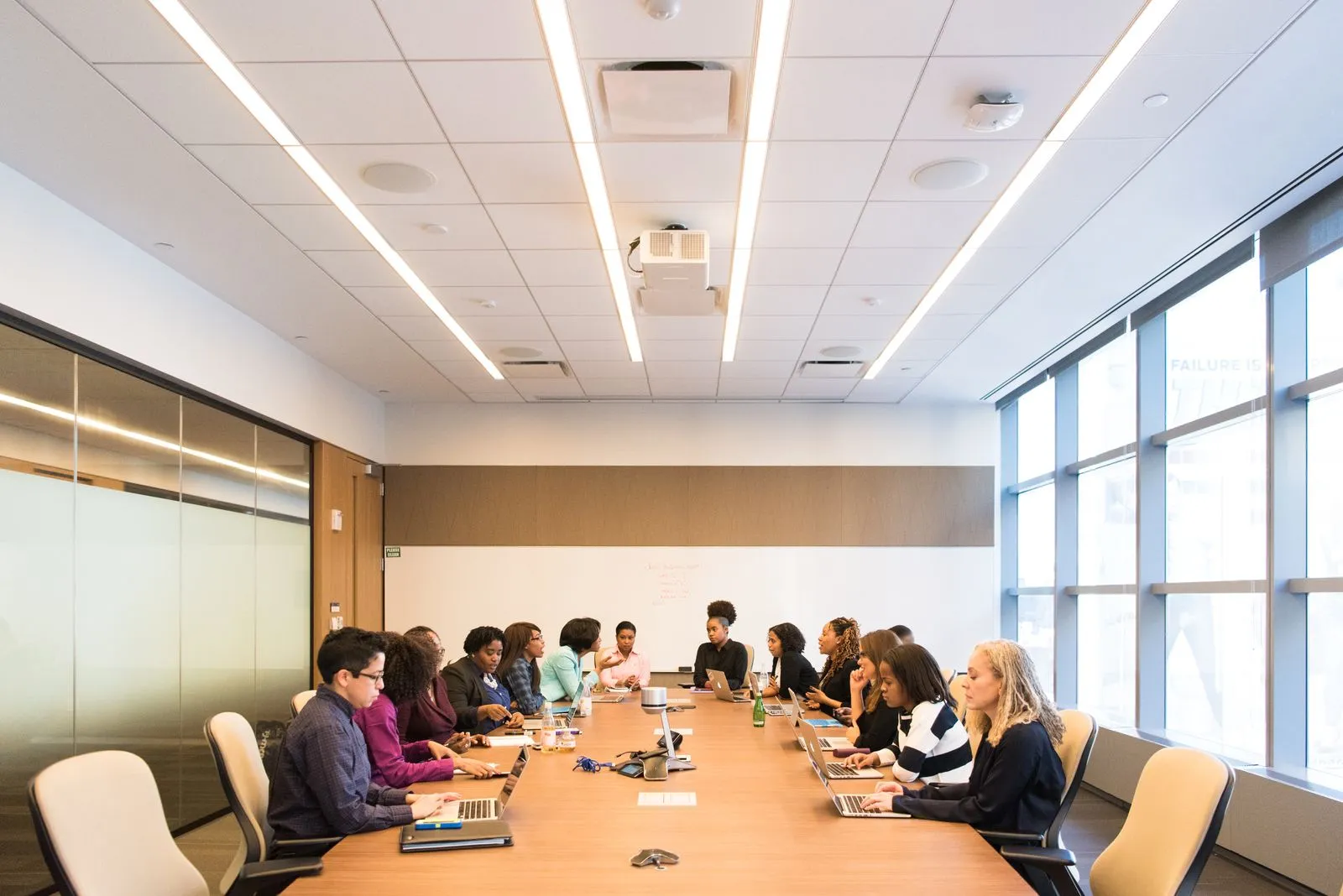 Large team seated around a long conference table with laptops in a bright meeting room