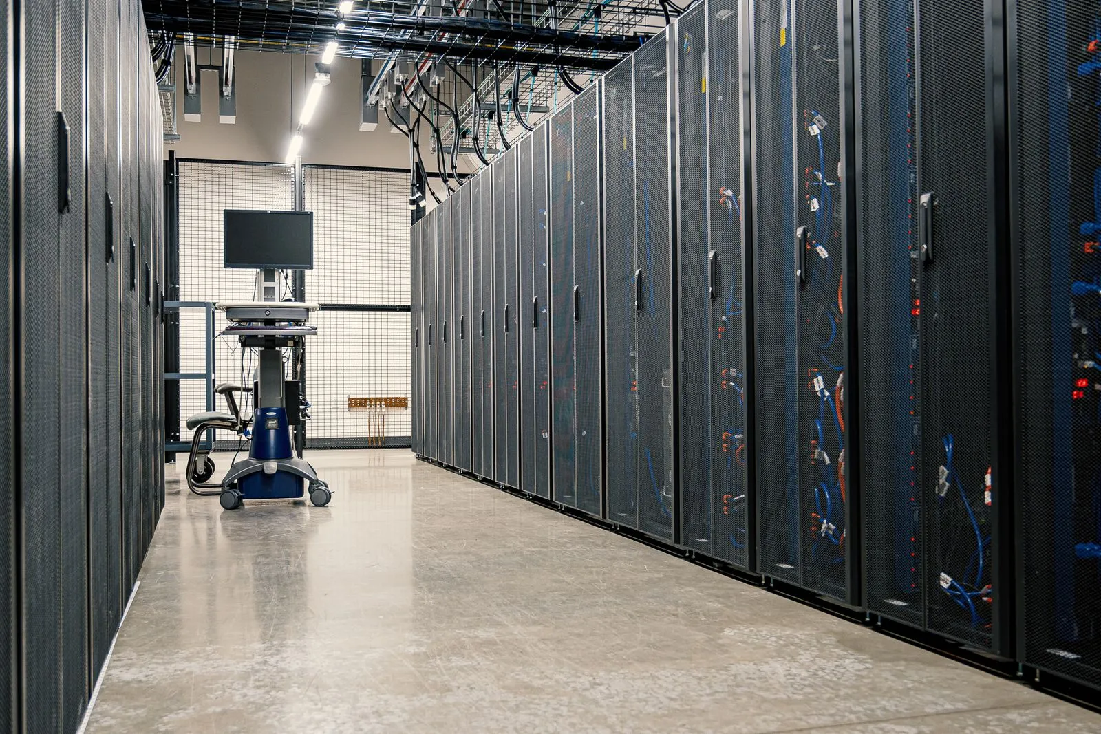 Data center aisle lined with server racks and a wheeled monitor cart