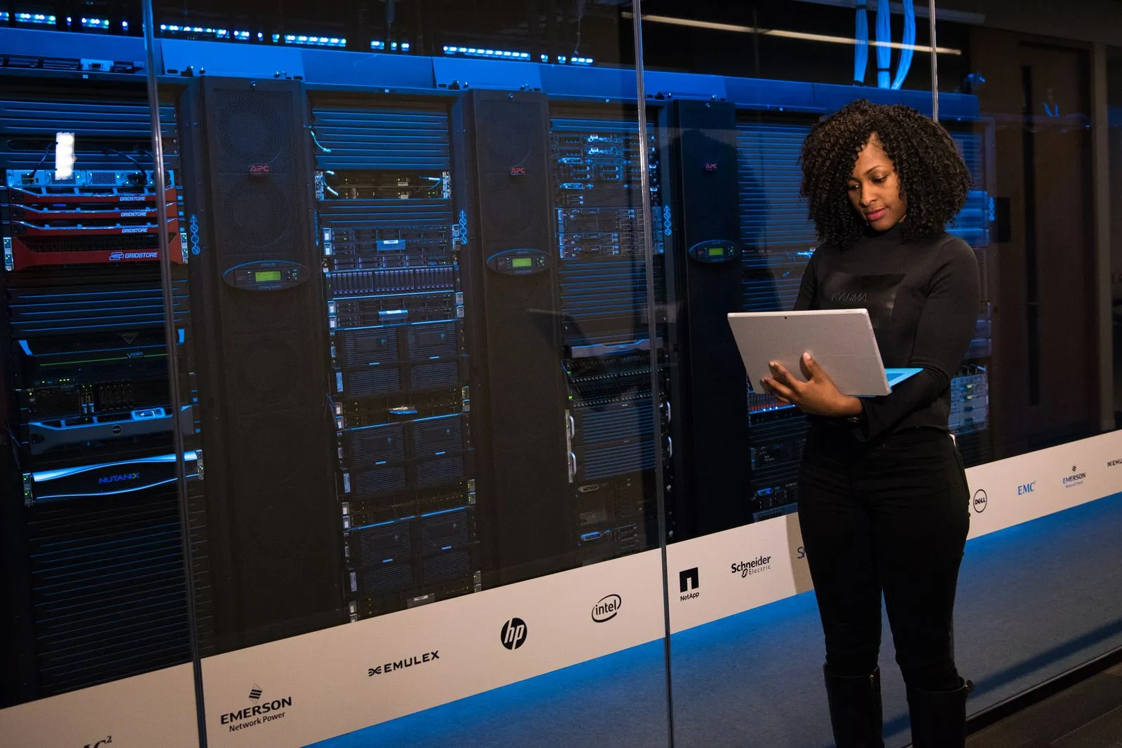 Woman holding a tablet in front of illuminated server racks at a technology expo booth