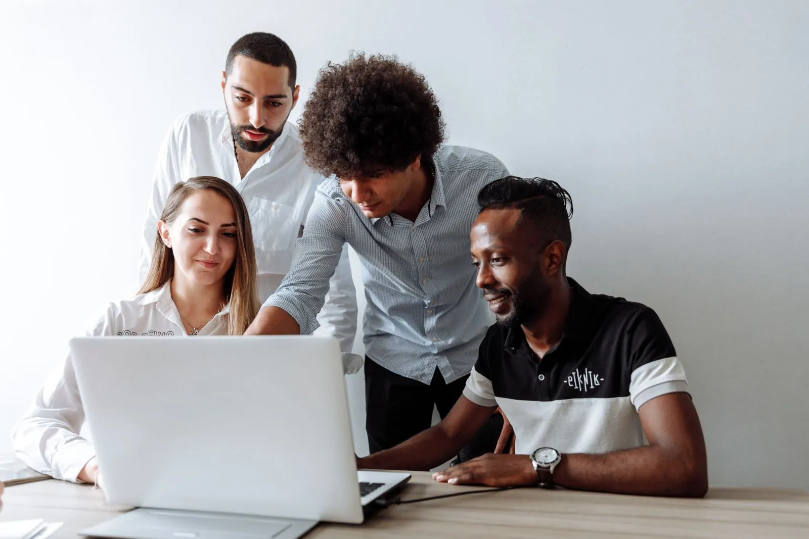 Four coworkers gather around a laptop, one seated and typing while three others look on