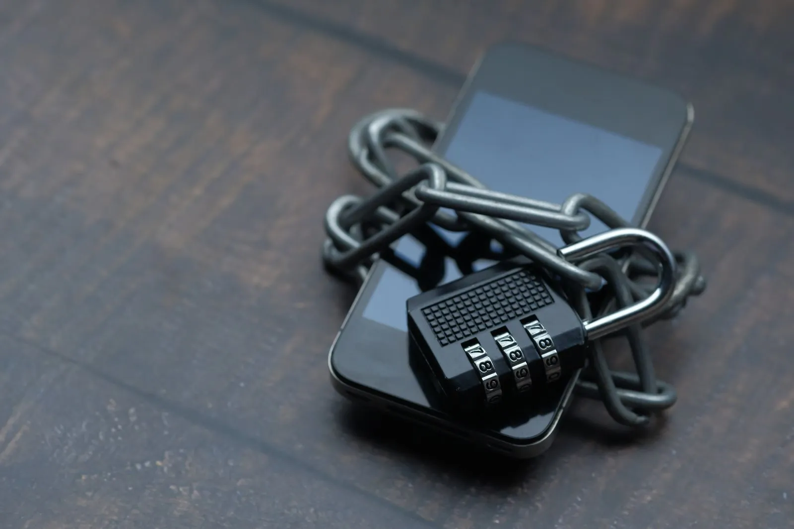 Two smartphones bound together with a chain and combination padlock on a wooden table