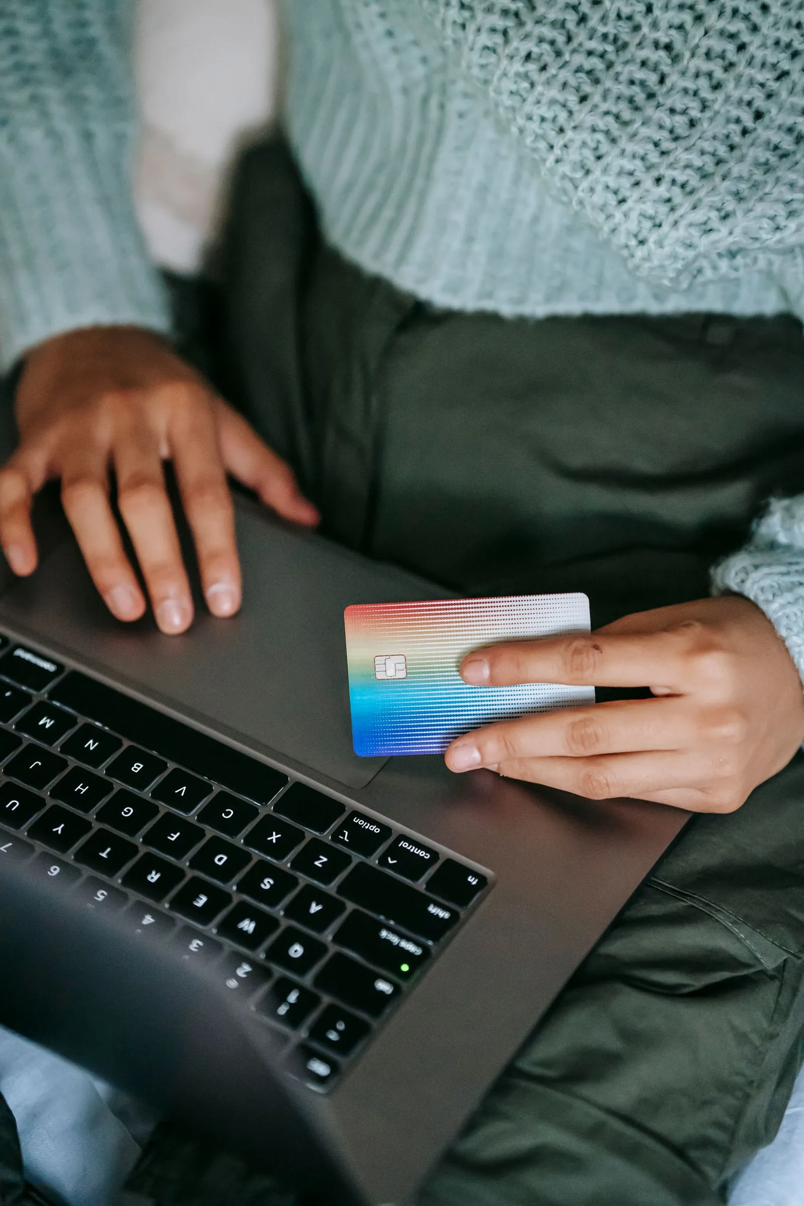Close-up of a hand holding a credit card beside an open laptop keyboard