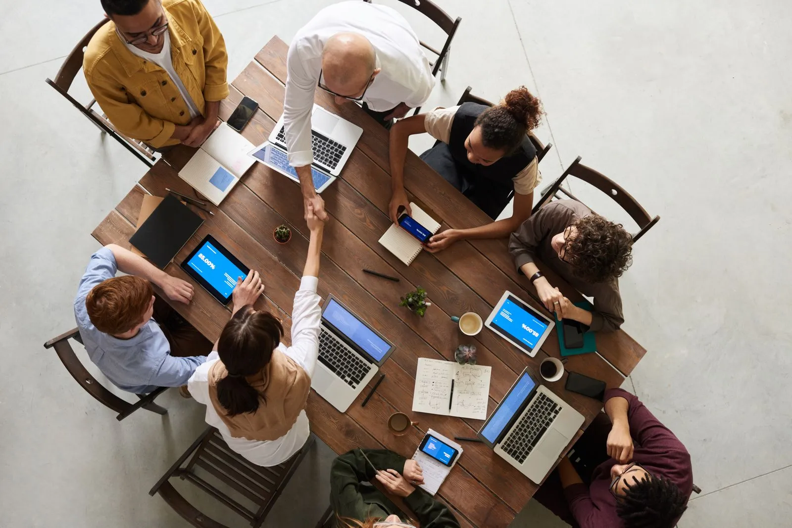 Overhead view of a team at a table with laptops, two people shaking hands