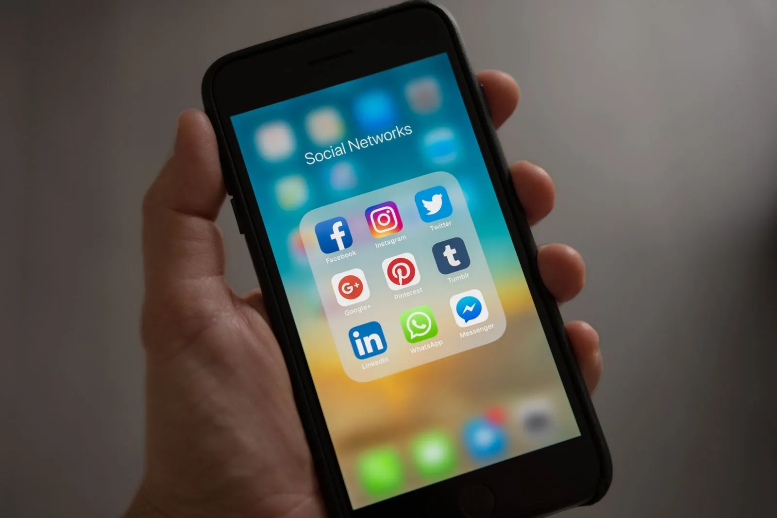 Hand holding a phone with a folder of social media app icons open on the home screen