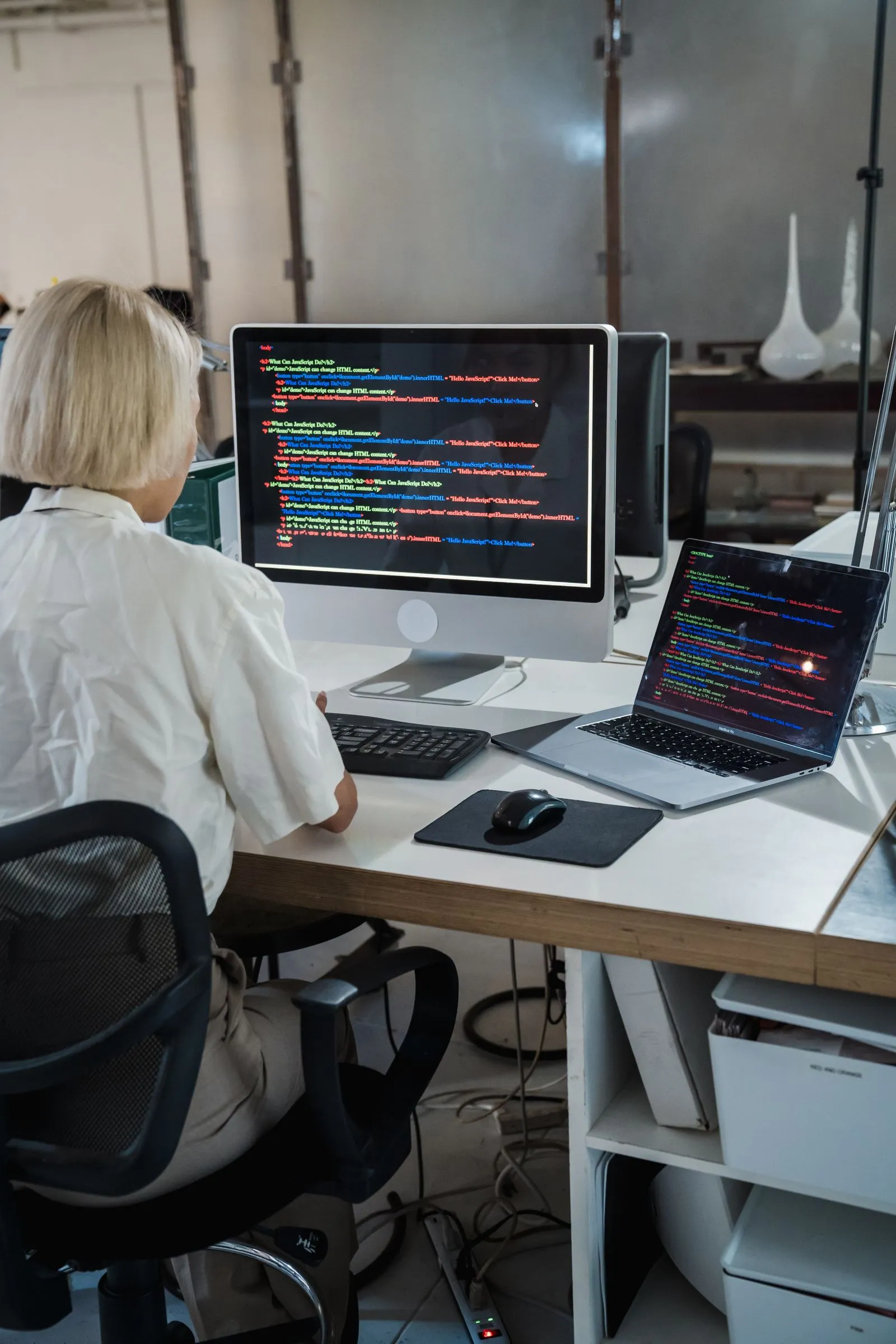 Woman viewing HTML and JavaScript code on an iMac and MacBook Pro side by side