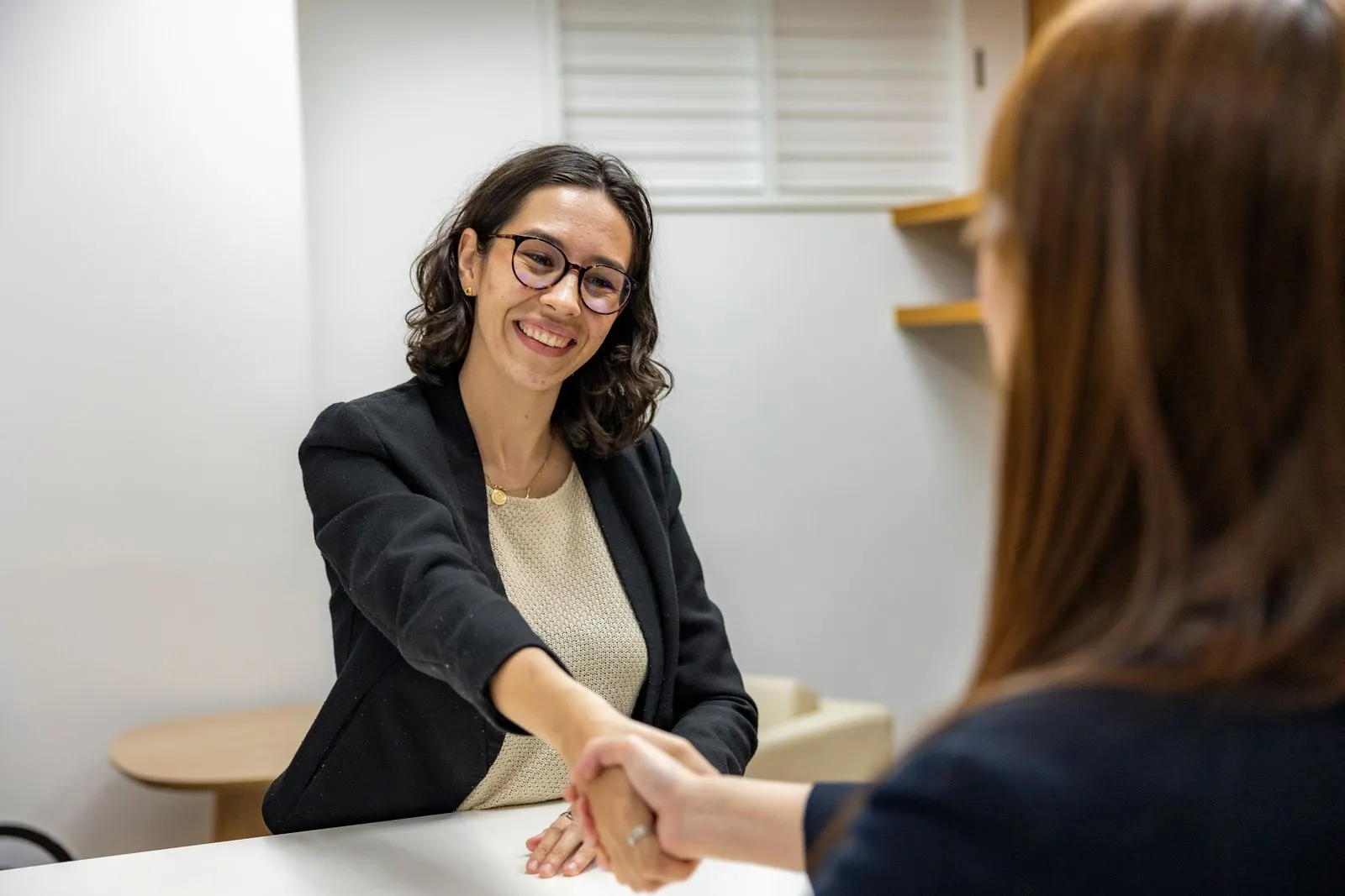 Two women shaking hands and smiling across a desk during an office interview