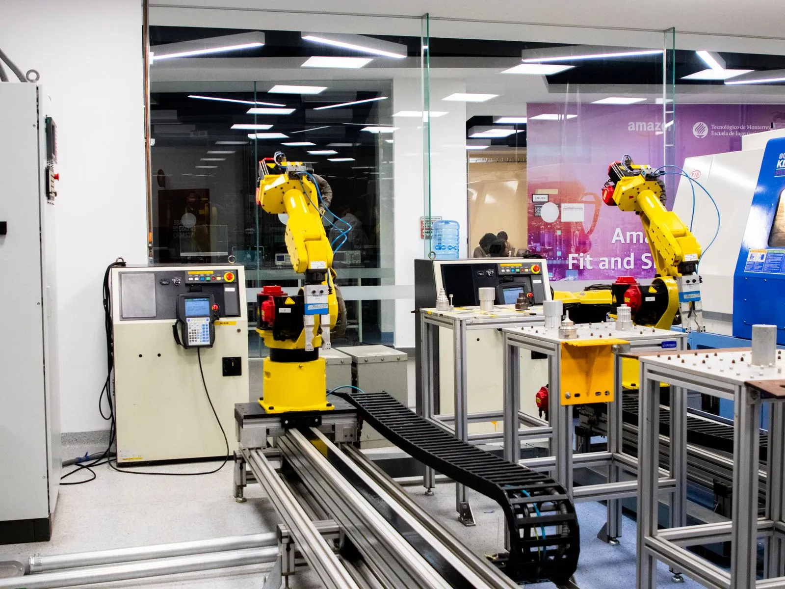 Yellow robotic arms and control panels in an automation lab, with an Amazon-branded banner behind