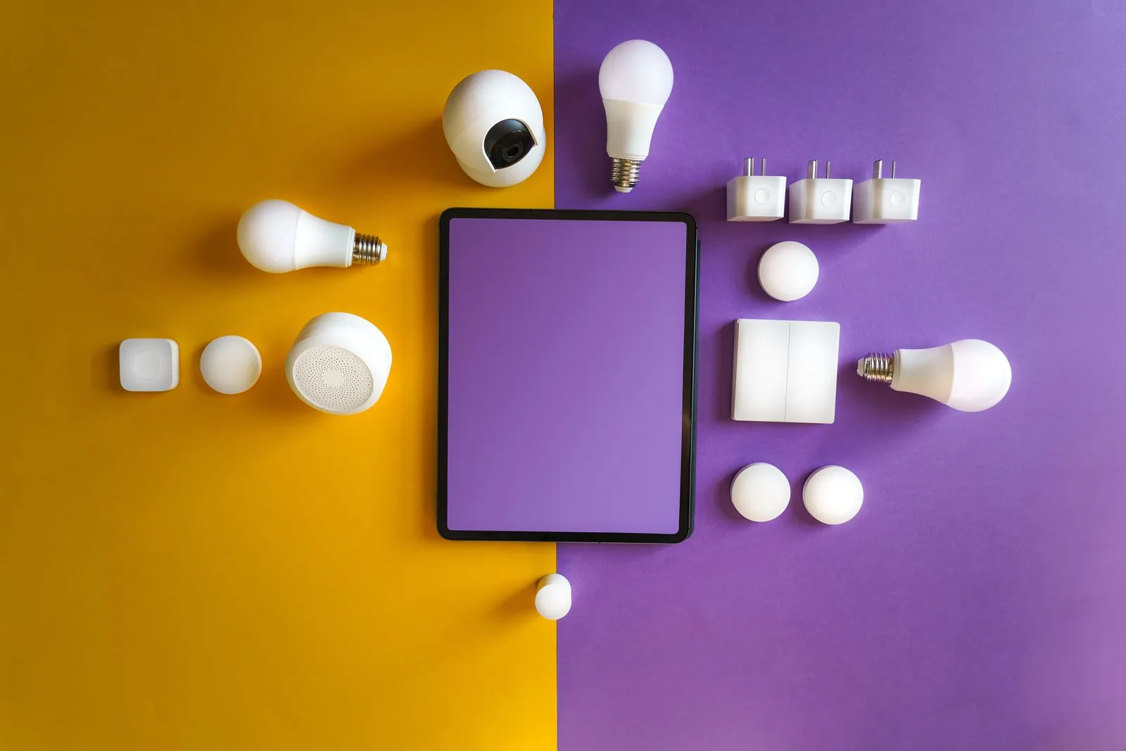 Flat lay of smart bulbs, cameras, and plugs arranged around a blank tablet on yellow and purple backgrounds