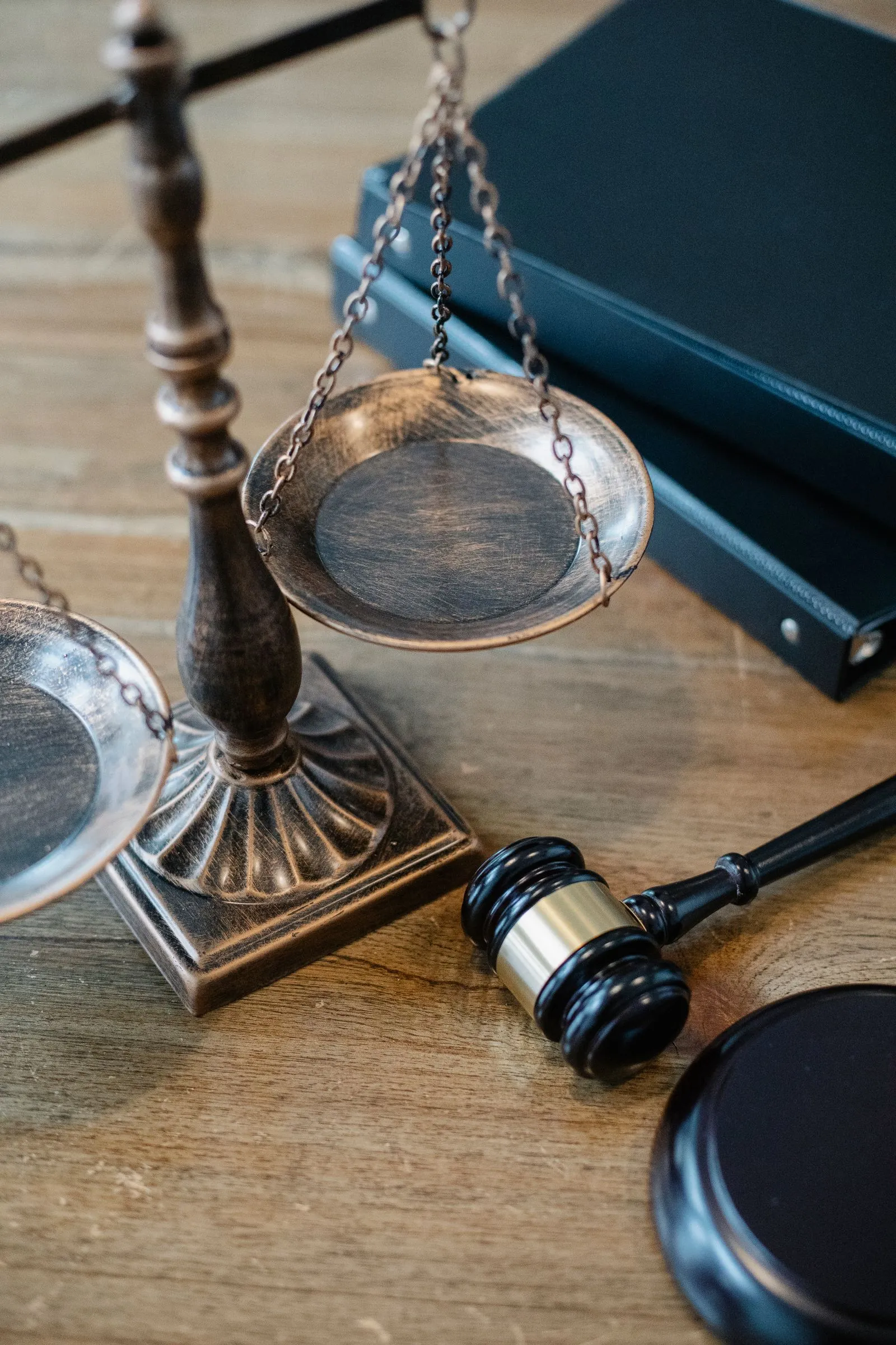Brass scales of justice and a wooden gavel resting beside a dark book on a wood table