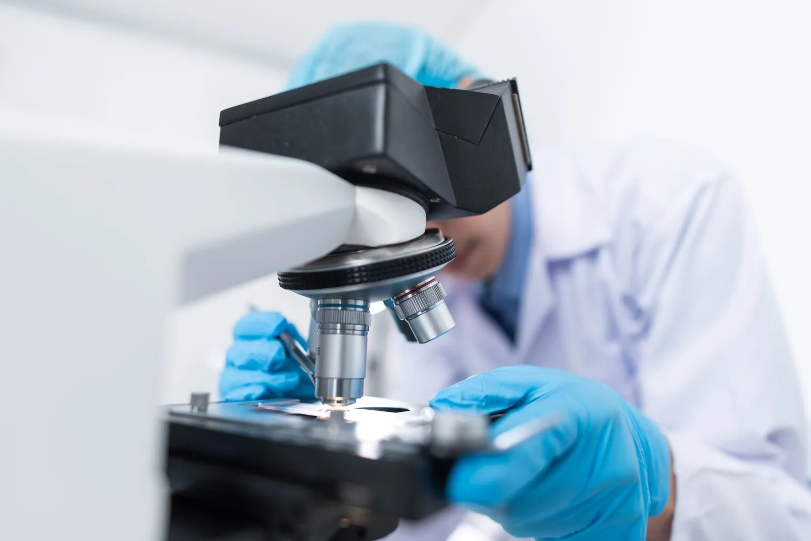 Gloved researcher in a lab coat peering into a microscope eyepiece