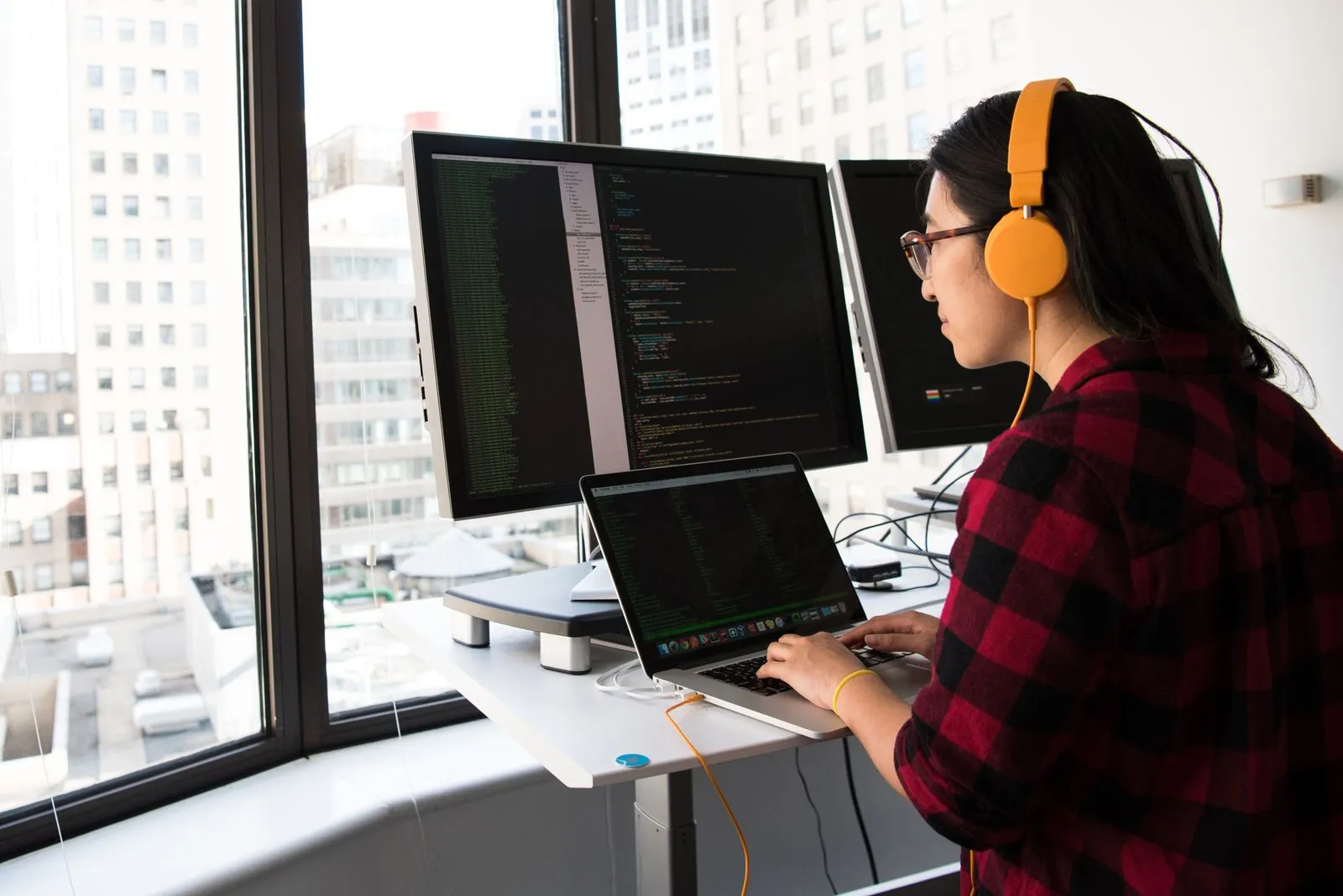 Woman wearing orange headphones typing at a standing desk with a city skyline view