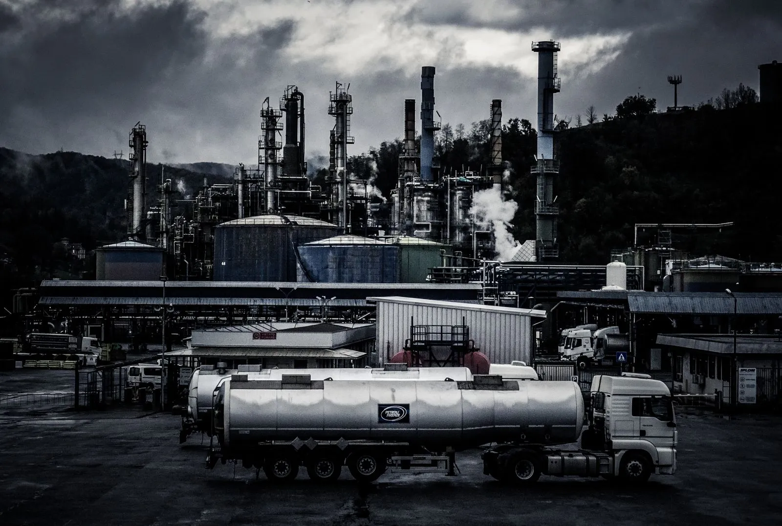 Fuel tanker truck parked in front of a smoking industrial refinery at dusk