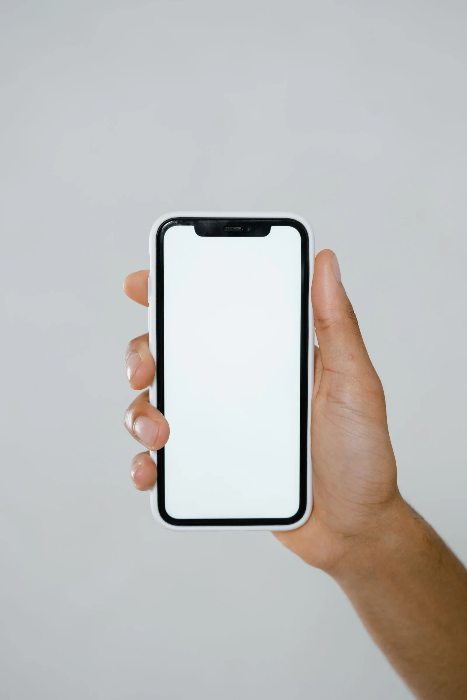 Hand holding a phone with a blank white screen against a plain gray background