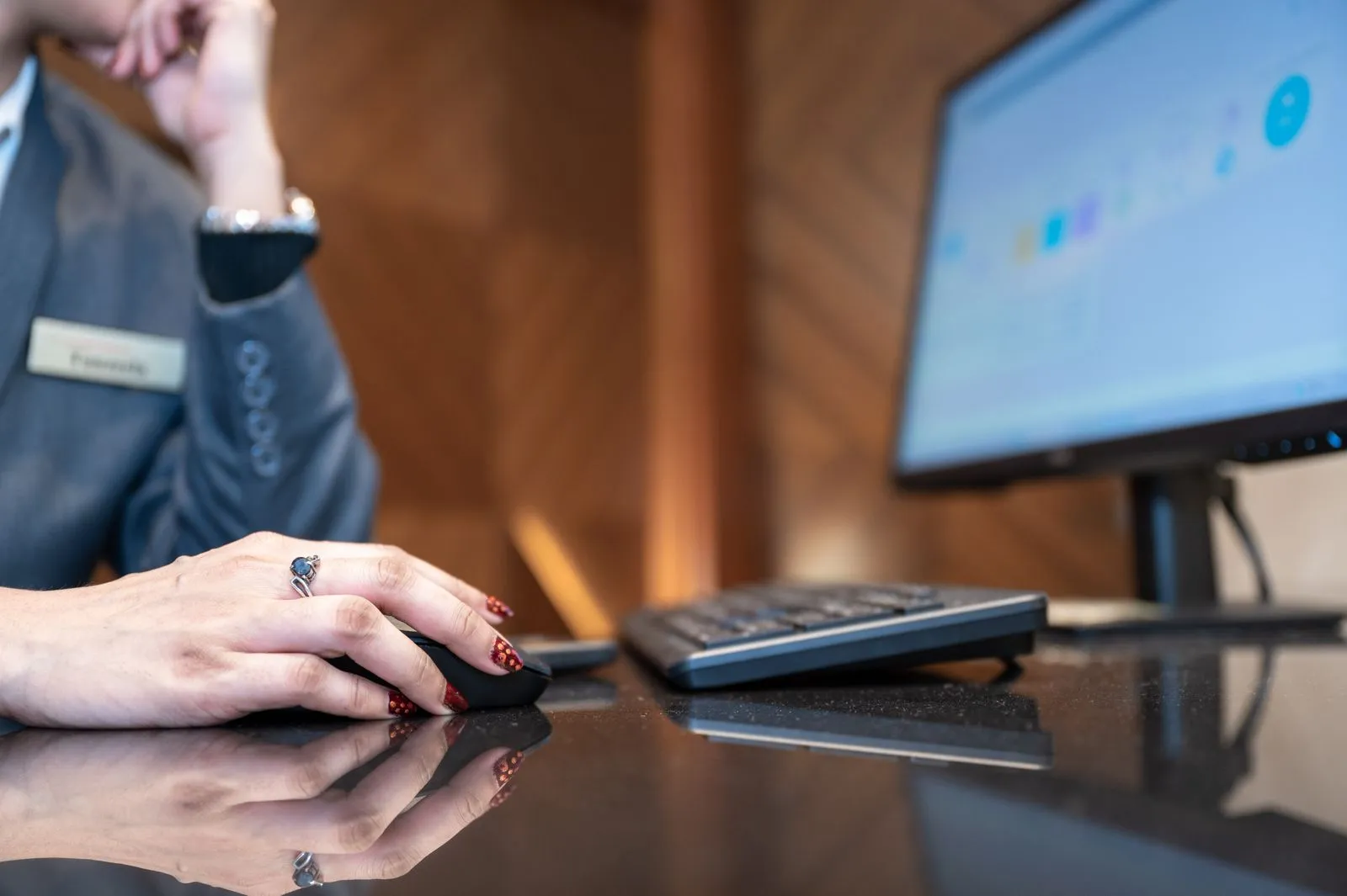 Close-up of a hand with red nail polish using a mouse near a blurred dashboard screen