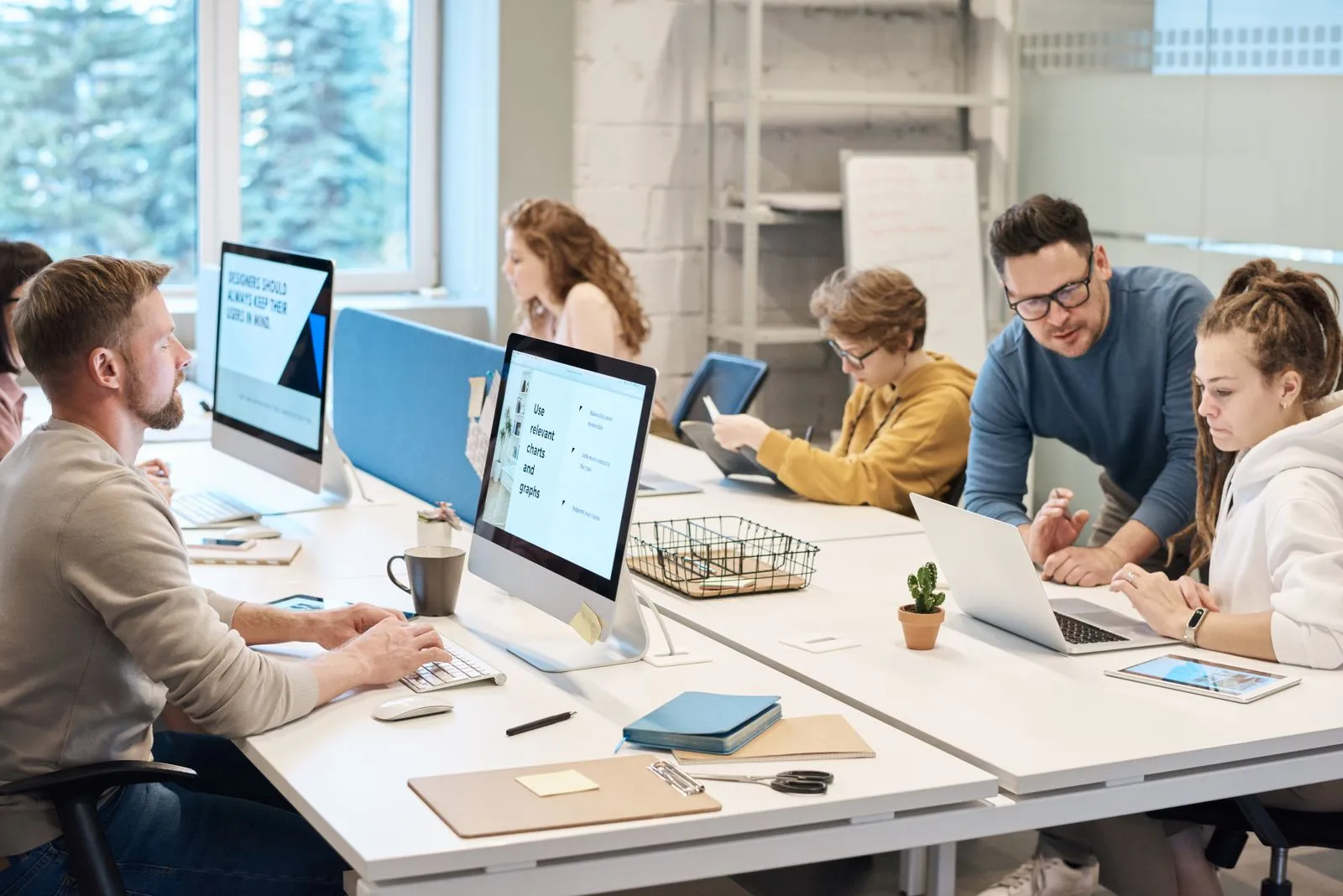 Coworkers at iMac workstations with a screen reading 'Use relevant charts and graphs'