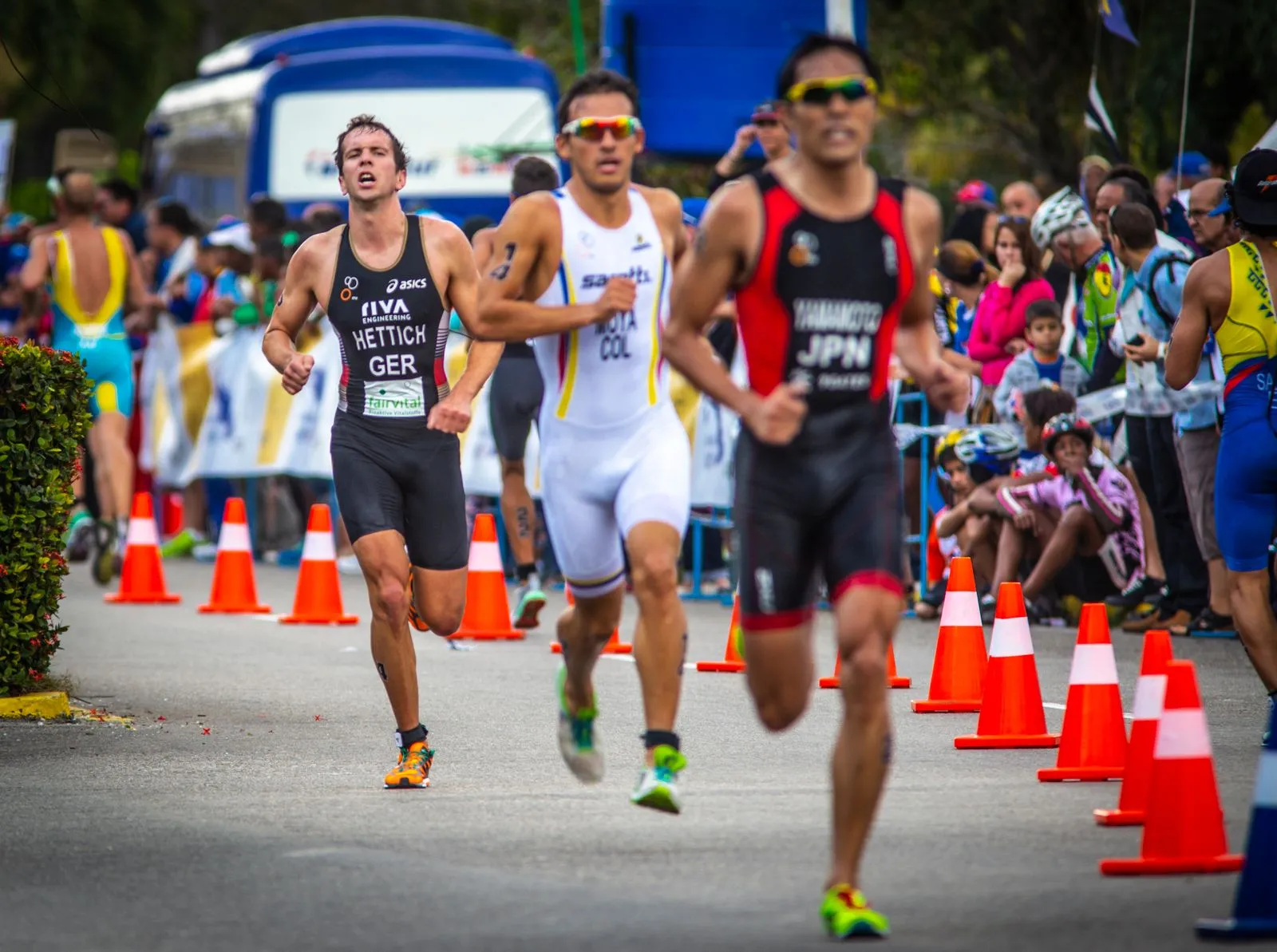 Triathletes racing past orange cones on a course lined with spectators