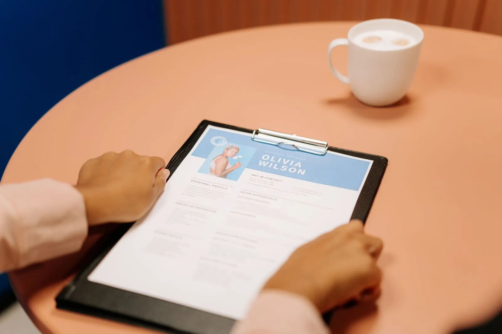 Overhead view of hands holding a clipboard resume for 'Olivia Wilson, Software Engineer' beside a latte
